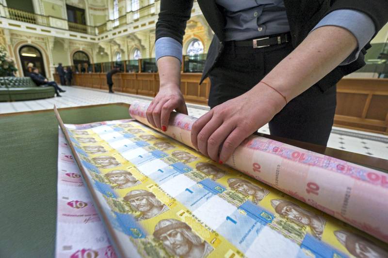 A bank worker rolls up uncut sheets of ten and one hryvnia banknotes after arranging for a photograph at the headquarters of the National Bank of Ukraine in Kiev, Ukraine, on Tuesday, March 22, 2016.  Ukraine's political gridlock, already holding up billions of dollars in aid, is also threatening financial stability and postponing monetary easing, according to the nations central bank governor. Photographer: Vincent Mundy/Bloomberg