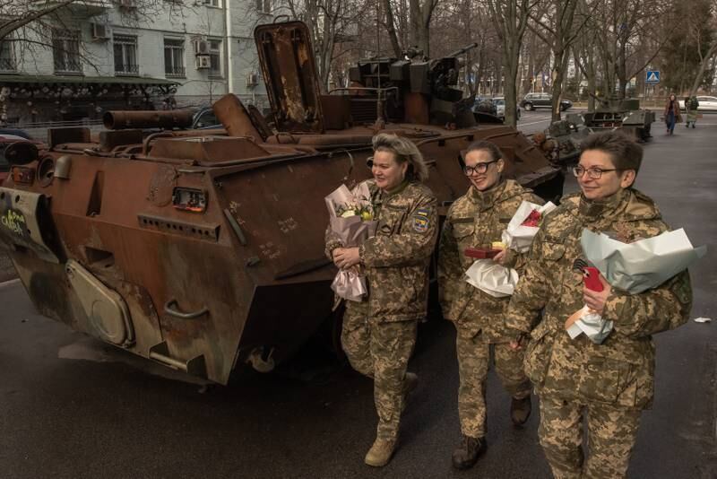 Ukrainian female soldiers hold awards and flowers received from President Volodymyr Zelensky as they walk past a destroyed Russian tank, in Kyiv, Ukraine. Getty 