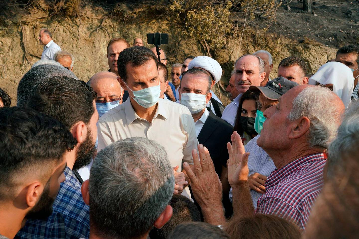 In this photo released Tuesday, Oct. 13, 2020 on the official Facebook page of the Syrian Presidency, Syrian President Bashar Assad, center, wearing a mask to help prevent the spread of the coronavirus, speaks with people during his visit to the coastal province of Latakia, Syria. Assad made a rare public visit to Latakia where he toured areas that suffered heavy damage in last weekâ€™s deadly wildfires. (Syrian Presidency via Facebook via AP)