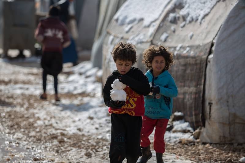 A displaced child carrying a piece of snow walks next to his sister through the camp in northern Syria.