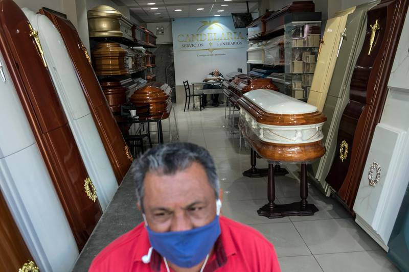 Raul Gonzalez, 59, wearing a protective face mask, waits for clients at the entrance of the Candelabra funeral home in Lima, Peru, as his boss Epifanio Gizaldo naps in the background. Business has fallen for funeral homes that specialise in selling coffins for victims of violent crime since the nationwide quarantine to help curb the spread of the new coronavirus. AP / Rodrigo Abd