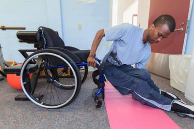 Man who had Spinal Meningitis getting into his wheelchair from yoga pad. Getty Images