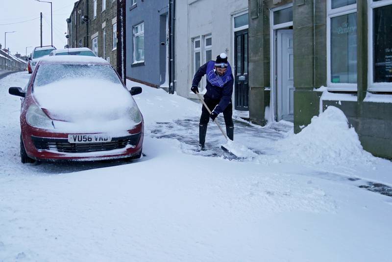 A man clears snow from the pavement in Tow Law, Co Durham. PA