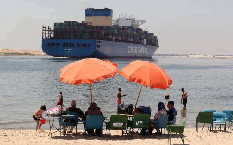 epa09232745 Egyptians swim in the Suez Canal as a container ship moves through it, in Ismaila, Egypt, 27 May 2021 (issued 28 May 2021). The Suez Canal Authority (SCA) chairman Osama Rabie, in an interview with EFE News Agency in Ismailia on the eve of the start of the compensation trial against the 'Ever Given' said that the black box indicated a serious fault of the captain because the center of the ship wasn't in the middle of the entrance and entered with a high speed that is not allowed in narrow sea lanes, which led to the accident that choked the canal and entered the ship 12 meters in the deep of the shore because of the high speed. Rabie also said that 'We are making a new 10 kilometers track to increase the number of passing ships and reduce the crossing time. And we're going to widen the canal 40 meters and increase the depth from 66 to 72 feet in the southern section' to prevent future accidents.  EPA/KHALED ELFIQI