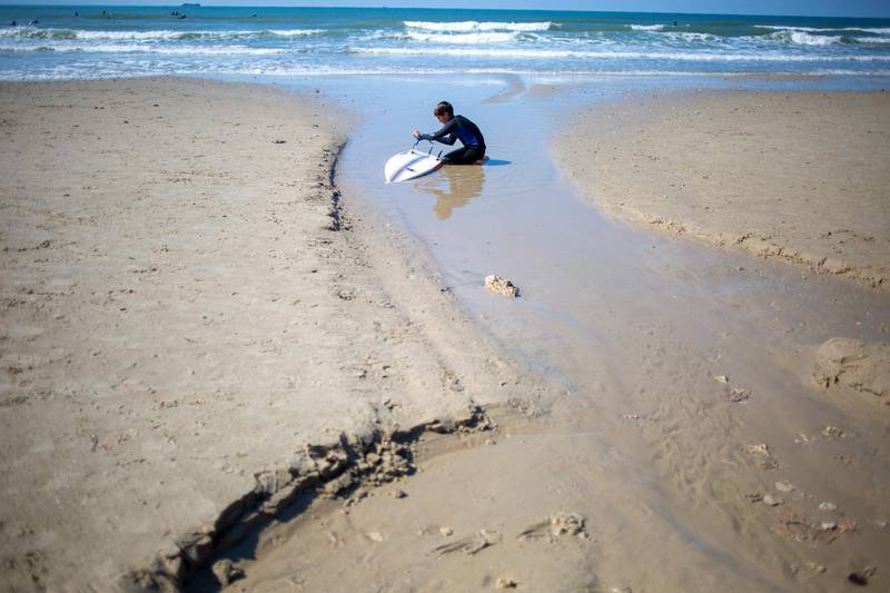 A surfer cleans his tar-covered surfboard at Gador nature reserve. AP