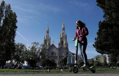 FILE - In this April 17, 2018 file photo, a woman rides a motorized scooter in Washington Square Park in San Francisco. Gov. Jerry Brown signed legislation Wednesday, Sept. 19, 2018, requiring helmets only for people under age 18 while riding motorized scooters. It's a win for companies such as Bird and Lime that operate the popular scooters in major cities across California and the country. (AP Photo/Jeff Chiu, File)