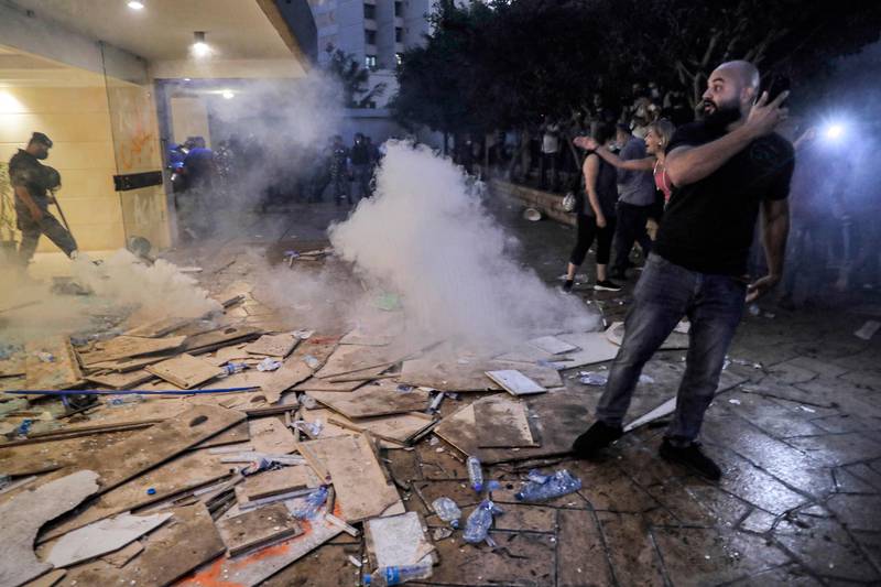 A protester stands next to tear gas fumes rising over broken, empty coffins brought by demonstrators and families of the Beirut blast victims, laid on the ground outside the entrance to the residence of Lebanon's interior minister in the Qoraitem neighbourhood of western Beirut.