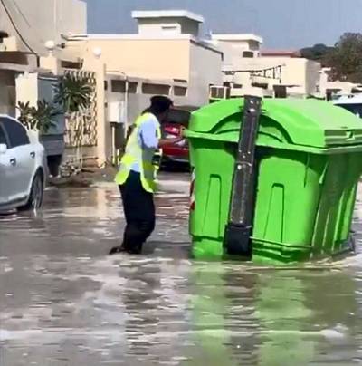 A police officer wades through flood water as he tries to clear a rubbish bin from the middle of a residential road in Kalba on Sharjah's east coast. Courtesy: Sharjah Police