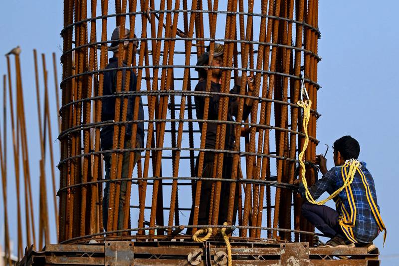 Labourers work on a pillar of an under-construction flyover along a road in New Delhi on February 15, 2022. (Photo by Money SHARMA / AFP)