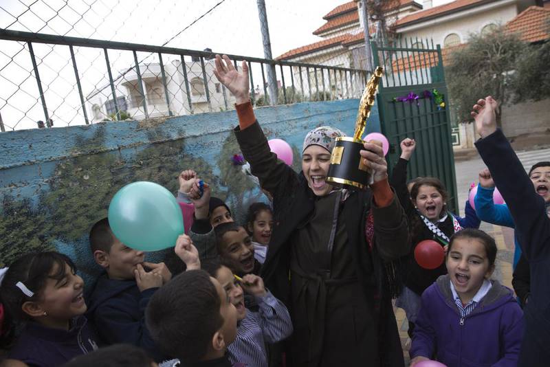 Palestinian teacher Hanan Al Hroub holds her 2016 Global Teacher trophy as her pupils greet her back to Samiha Khalil school in Al Bireh, just outside Ramallah. Heidi Levine For The National