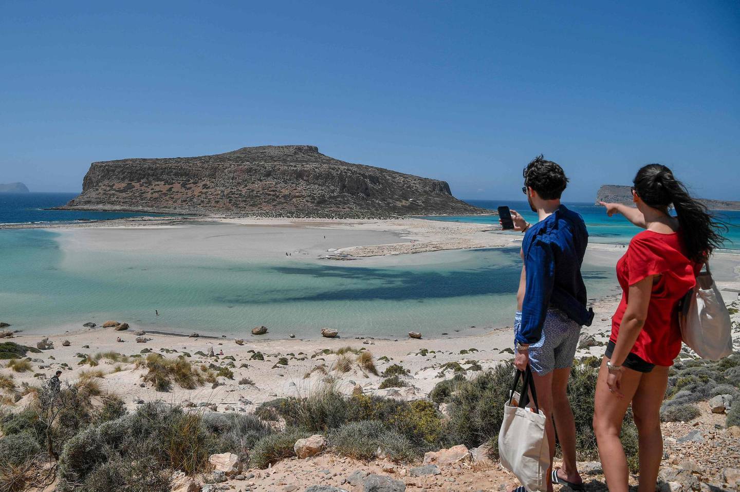 A couple of tourists looks at the Balos beach and its lagoon in the north west of the island of Crete, on May 13, 2021.

 Greece easies the Covid-19 measures in welcoming international tourists on May 14. / AFP / Louisa GOULIAMAKI

