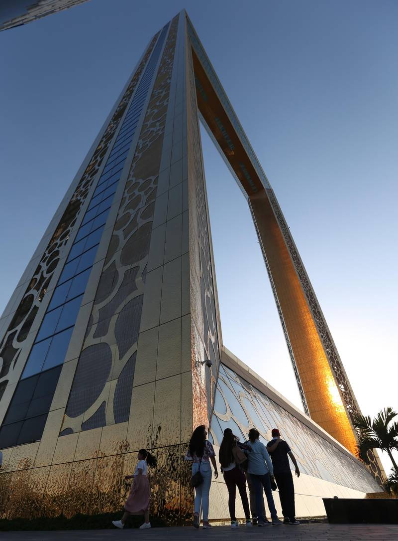epa07710665 People walk past the world's largest picture frame building called Dubai Frame at Zabeel Park in the Gulf emirate of Dubai, United Arab Emirates, 11 July 2019. The Dubai Frame is a structure that 'frames' views of Old and New Dubai. The Frame's dimensions are 150 meters high and 93 meters wide, and were used over 9,900 cubic meters of reinforced concrete, 2,000 tons of steel and 2,900 square meters of laminated glass to construct it. More than 15,000 square meters of gold-colored stainless steel covers Dubai Frame, which incorporates a ring design inspired by the EXPO 2020 Dubai logo, and is using an elevator which is carrying visitors to 48 floors the Sky deck in 75 seconds.  EPA/ALI HAIDER