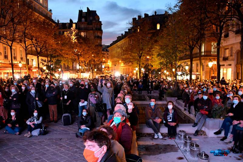 People gather on the Place de la Sorbonne in Paris on October 21, 2020, to watch a live broadcast on a giant screen of a national homage at the Sorbonne University to French teacher Samuel Paty, who was beheaded for showing cartoons of the Prophet Mohamed in his civics class.  AFP