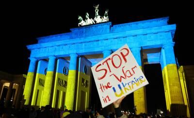 A protest banner outside Brandenburg Gate in Berlin, which is also lit up in the colours of the Ukrainian flag. Reuters