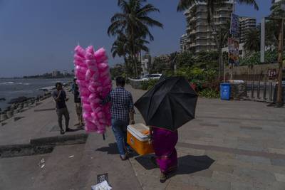 A man selling candy floss in Mumbai helps a water vendor who is using an umbrella as a parasol. AP
