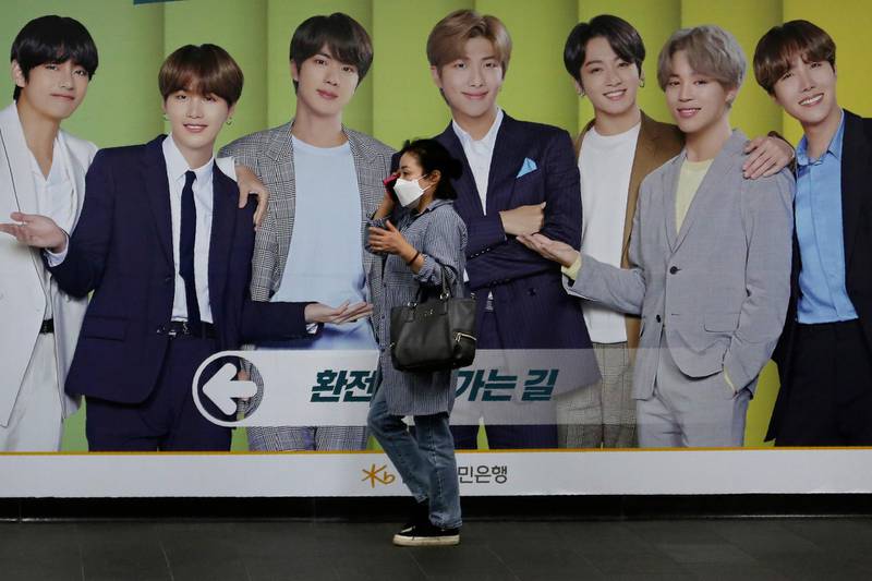 A woman walks by a board showing members of BTS to advertise a local bank's money exchange in Seoul, South Korea. AP Photo