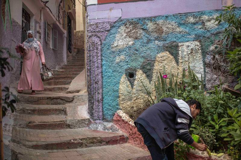 A man paints outside his home while a woman wearing a face mask walks past during a health state of emergency and home confinement order in Rabat, Morocco. AP Photo