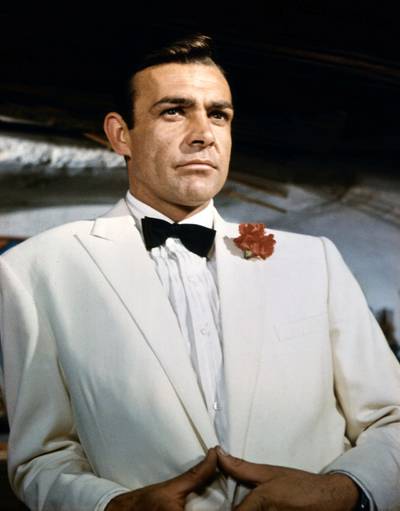 (Original Caption) ca. 1966: Waist-up portrait of Sean Connery, as James Bond, leaning against a bar and looking out across the room. Connery is wearing a white tuxedo and bow tie with a red carnation in his lapel. CONNERY; SEAN BOND; JAMES. 99/99/1966 35 U CT4X5