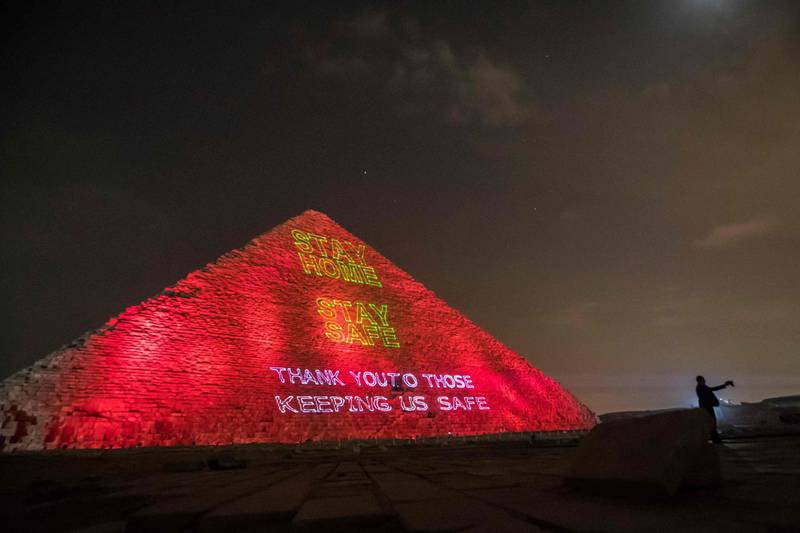A man takes a selfie in front of the Great pyramid of Kheops where a laser projection writes "Stay at home, stay safe" on March 30, 2020, amid the spread of the COVID-19 infection, caused by the novel coronavirus. / AFP / Khaled DESOUKI
