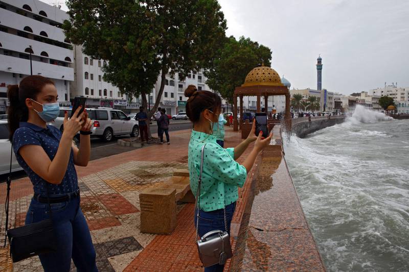 Women take pictures of high waves breaking on the seaside promenade in the Omani capital.