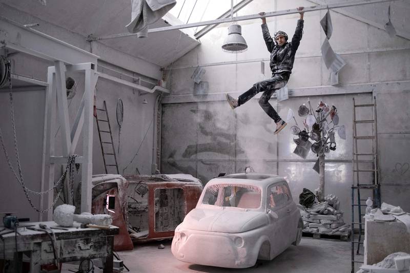 Italian artist Nazareno Biondo hangs out above his sculpture made from Carrara marble representing the iconic Fiat 500 car. AFP