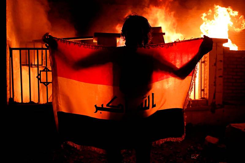 A man holds a national flag while protesters burn the municipal complex during protests in Basra. AP Photo