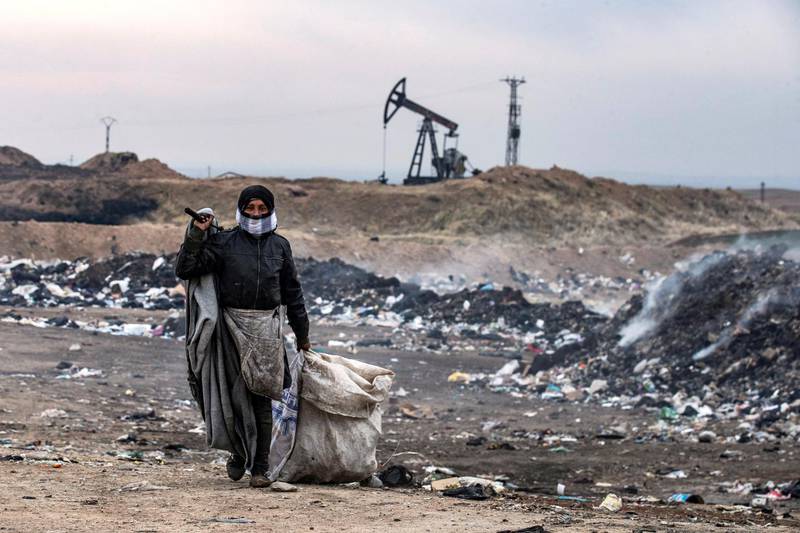 A Syrian man sifts through a garbage dump in the countryside of Malikiya in northeast Syria, on January 17, 2021. - On the dry plains outside the city of Al-Malikiyah, a dozen people wrapped up against the cold rip open the black plastic bags, in a desperate search for something to sell, repurpose or even eat. Across the road, an oil pump swings back and forth in this resource-rich region controlled by US-backed Kurdish forces. (Photo by Delil SOULEIMAN / AFP)