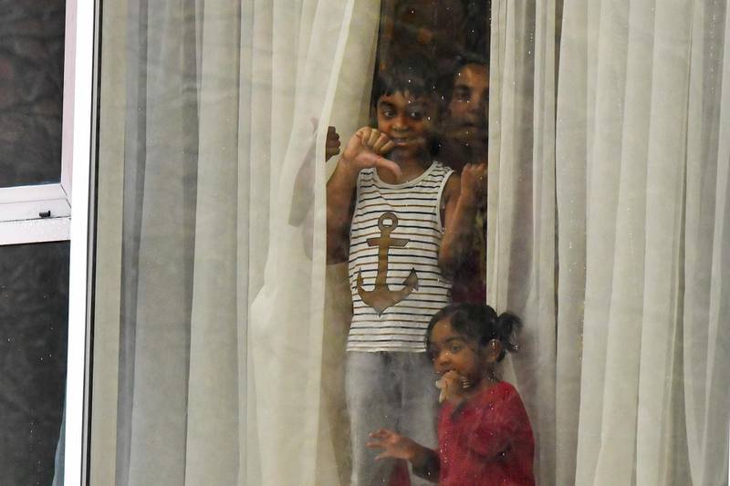 A woman accompanied by a boy and girl stand and gesture out of a window from inside the Radisson Blu hotel at Heathrow Airport, where they are undertaking mandatory quarantine. AFP
