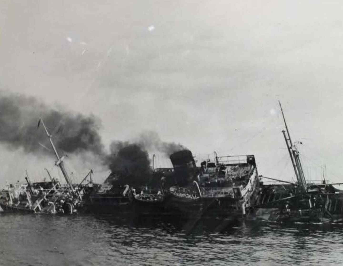 Listing heavily and her deck already partly submerged, the Dara begins to sink while under tow to Dubai, The ship was still burning two days after a bomb caused a fire that killed at least 240 people on April 8, 1961. UK National Archives