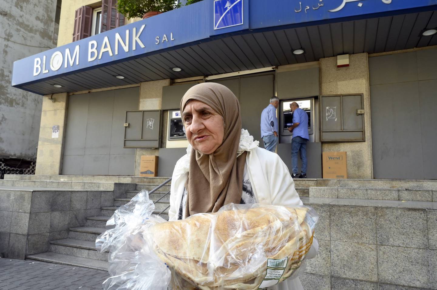 A woman carries bread as she walks past a closed bank in Beirut. Photo: EPA 