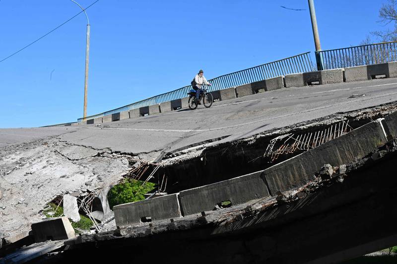 A man rides his bicycle over a heavily damaged bridge near Pechenegi village in the Kharkiv region, amid the Russian invasion of Ukraine. AFP