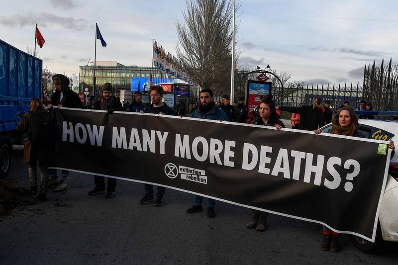 Activists from international climate action group Extinction Rebellion hold a banner reading "how many more deaths?" after dumping manure outsideCOP25. AFP