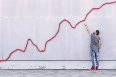 A red bar line graph rises like a financial graph or graphic with a young man pointing at the growth against a wall