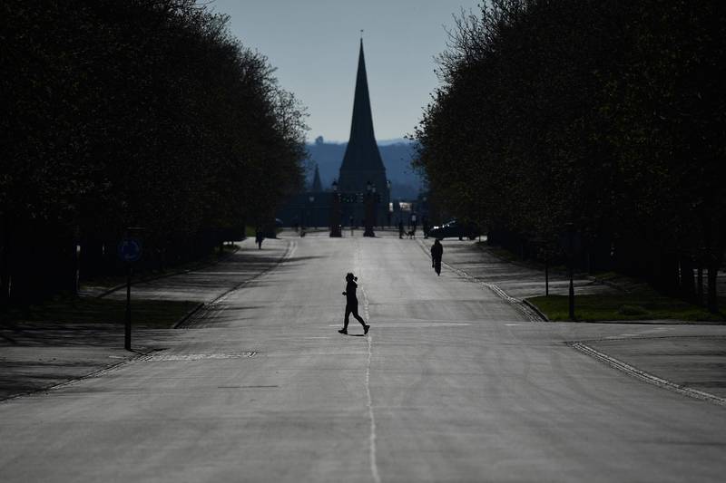 This picture taken on March 23, 2020 shows a runner crossing a road closed to traffic as she exercises in Greenwich Park in south London, as people come to terms with the government's request for social distancing as a preventive measure against the spread of the COVID-19 novel coronavirus. / AFP / Ben STANSALL
