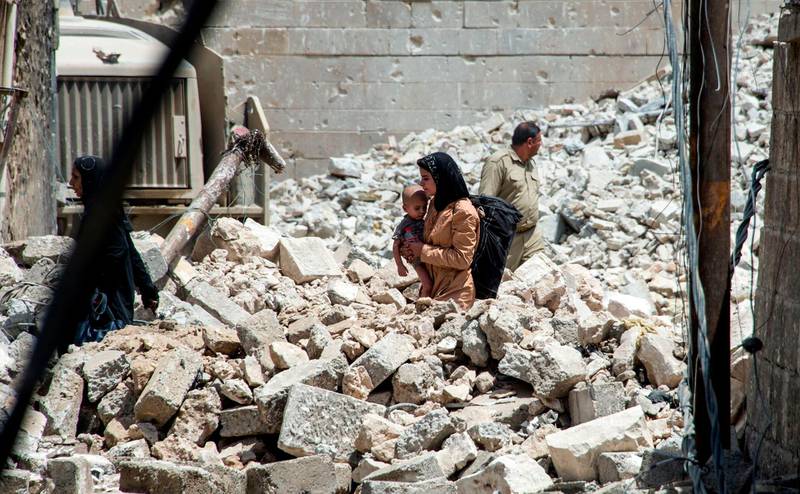 (FILES) In this file photo taken on July 02, 2017 An Iraqi woman carries a child as she walks through the rubble in the Old City of Mosul on July 2, 2017, during the offensive to retake the city from Islamic State (IS) group fighters. Iraqi forces announced the "liberation" of the country's second city on July 10, 2017, after a bloody nine-month offensive to end the Islamic State (IS) group's three-year rule there. 
Scores of people are still displaced in and around Mosul as the city lies in ruins, one year after it was retaken from IS. 

 / AFP / Fadel SENNA
