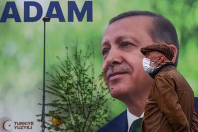 A man wearing a face mask stands in front of a huge poster with a picture of Turkish President Recep Tayyip Erdogan on the facade of a building, in Istanbul, Turkey, 10 May 2023. EPA