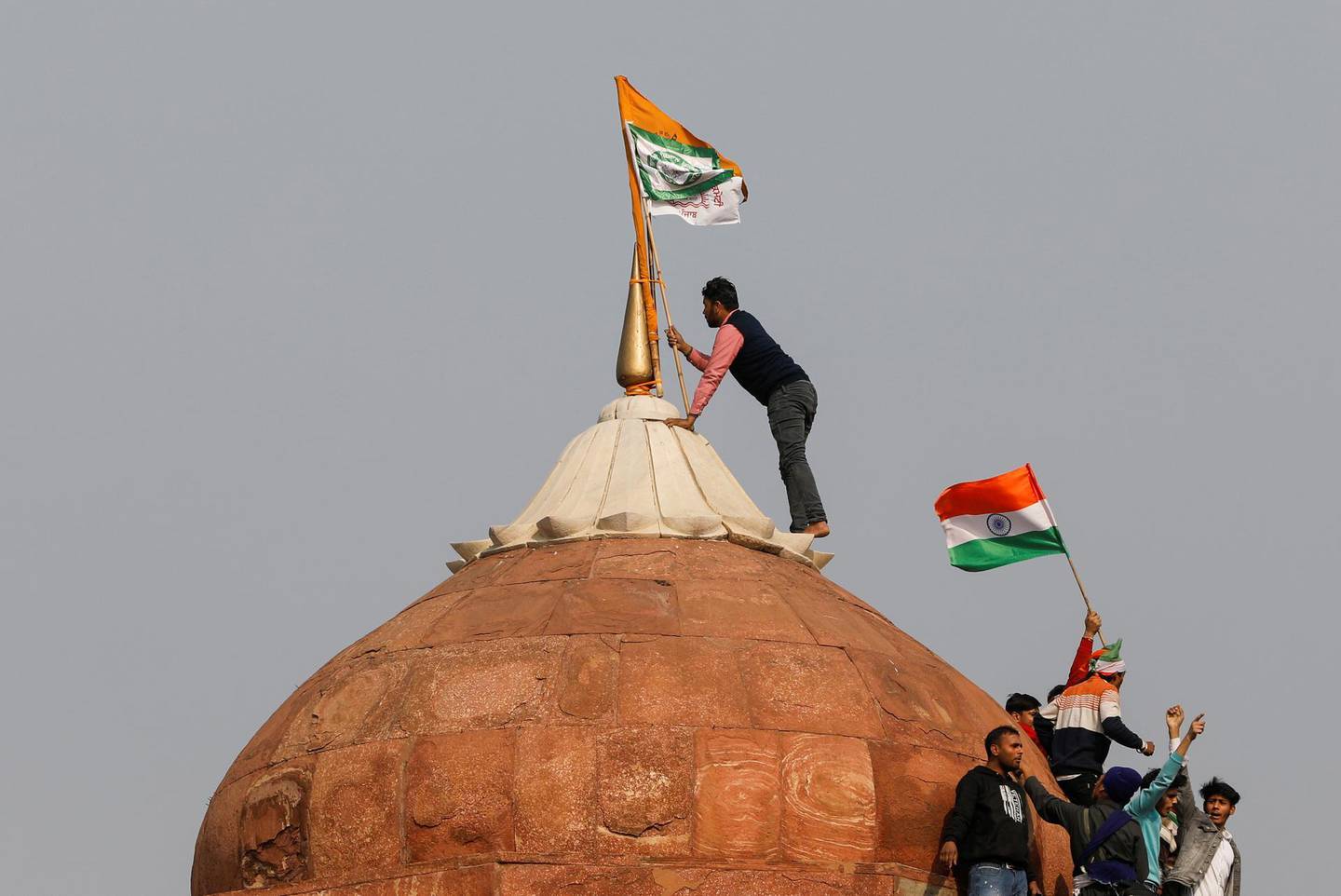A farmer puts a flag atop the historic Red Fort in Delhi, during a protest against farm laws introduced by the government. Reuters.