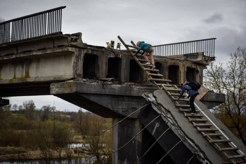 Natalia and her daughter climb a ladder, passing over a destroyed bridge in Kyiv. EPA