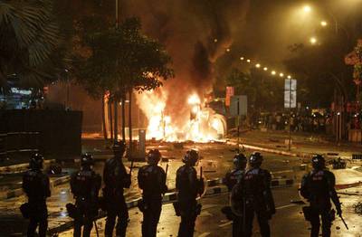 Riot police stand guard as a vehicle burns after a rare riot in Singapore on Monday. AP Photo