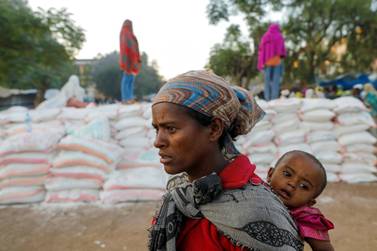 A woman carries an infant as she queues for food at a temporary shelter for people displaced by conflict, in the town of Shire in Ethiopia's Tigray region. Reuters
