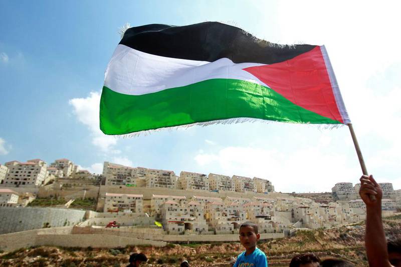A protester waves a Palestinian flag in front of the Israeli West Bank settlement of Beitar Illit on September 5, 2014, during a demonstration against Israel’s decision to expropriate 400 hectares of land in the territory. Musa Al Shaer / AFP