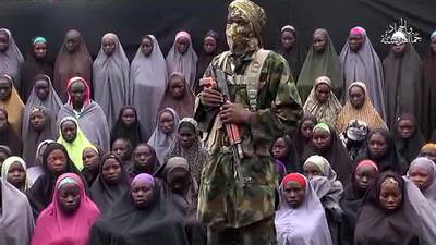 A video grab image created on August 14, 2016 taken from a video released on youtube purportedly by the Boko Haram group that claims to show one of its fighters at an undisclosed location standing in front of girls allegedly kidnapped from Chibok in April 2014. Boko Haram/AFP



