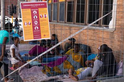 An information poster on the coronavirus is secured to a fence among refugees from various African nations living on a city sidewalk in Cape Town, South Africa, on March 23 2020. EPA