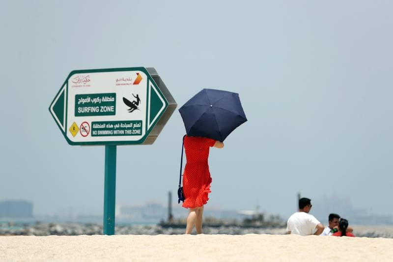 Dubai, United Arab Emirates - July 02, 2019: Tourists cover up on a very hot day at the beach. Tuesday the 2nd of July 2019. Jumeirah public beach, Dubai. Chris Whiteoak / The National