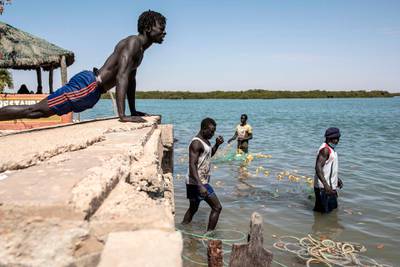A fisherman does push-ups as his colleagues get their fishing nets ready for their next trip in the protected wetlands area of Joal Fadiouth, in the Thies region of Senegal. AFP