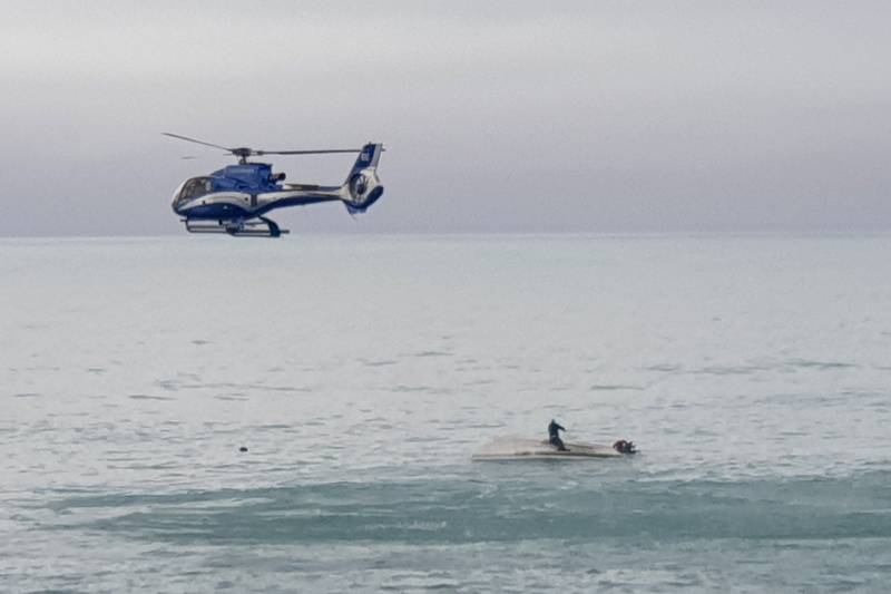 A helicopter flies overs an upturned boat with a survivor sitting on the hull, off the coast of Kaikoura, New Zealand, on Satruday. AP