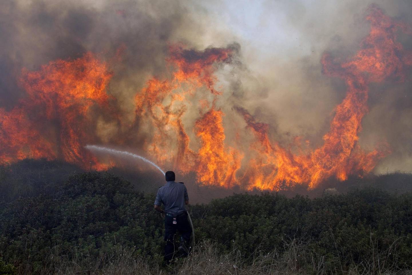 An Israeli fireman douses a brush fire in the vicinity of the Hadera power plant in northern of Israel, on September 7, 2011. AFP PHOTO/JACK GUEZ (Photo by JACK GUEZ / AFP)