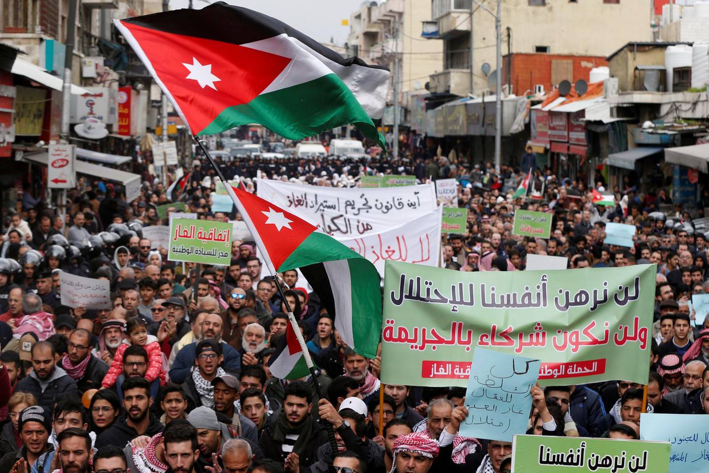 FILE PHOTO: Demonstrators hold Jordanian national flags and chant slogans during a protest against a government's agreement to import natural gas from Israel, in Amman, Jordan January 17, 2020. The placard reads: "We will not mortgage ourselves to the occupation, and we will not be complicit in the crime". REUTERS/Muhammad Hamed/File Photo