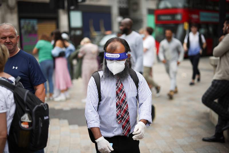 A person wearing a protective face shield and face mask walks through Oxford Circus in London.