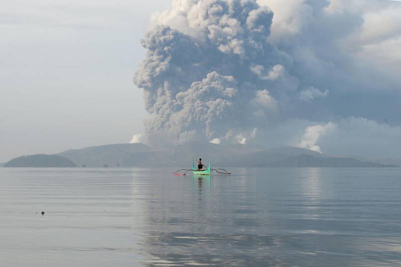 A youth living at the foot of Taal volcano rides an outrigger canoe while the volcano spews ash as seen from Tanauan town in Batangas. AFP